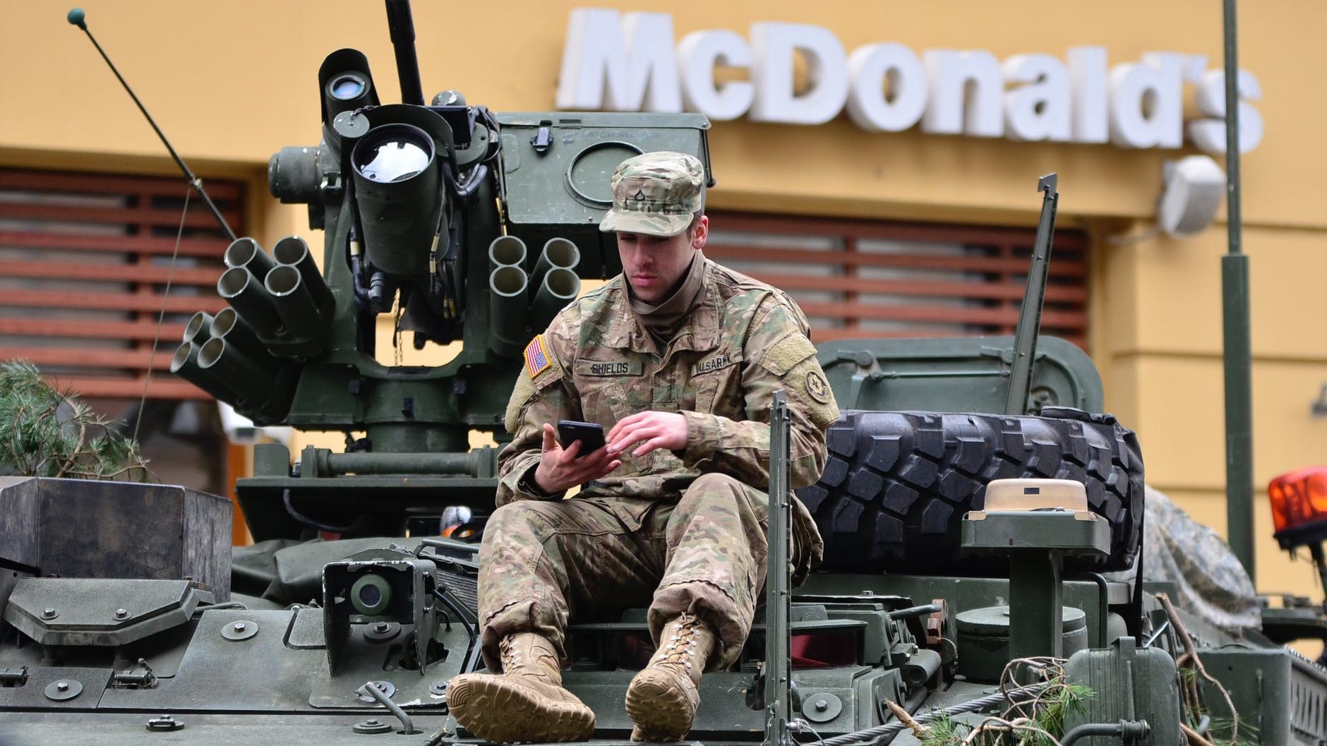 man in brown camouflage sitting on top of tank