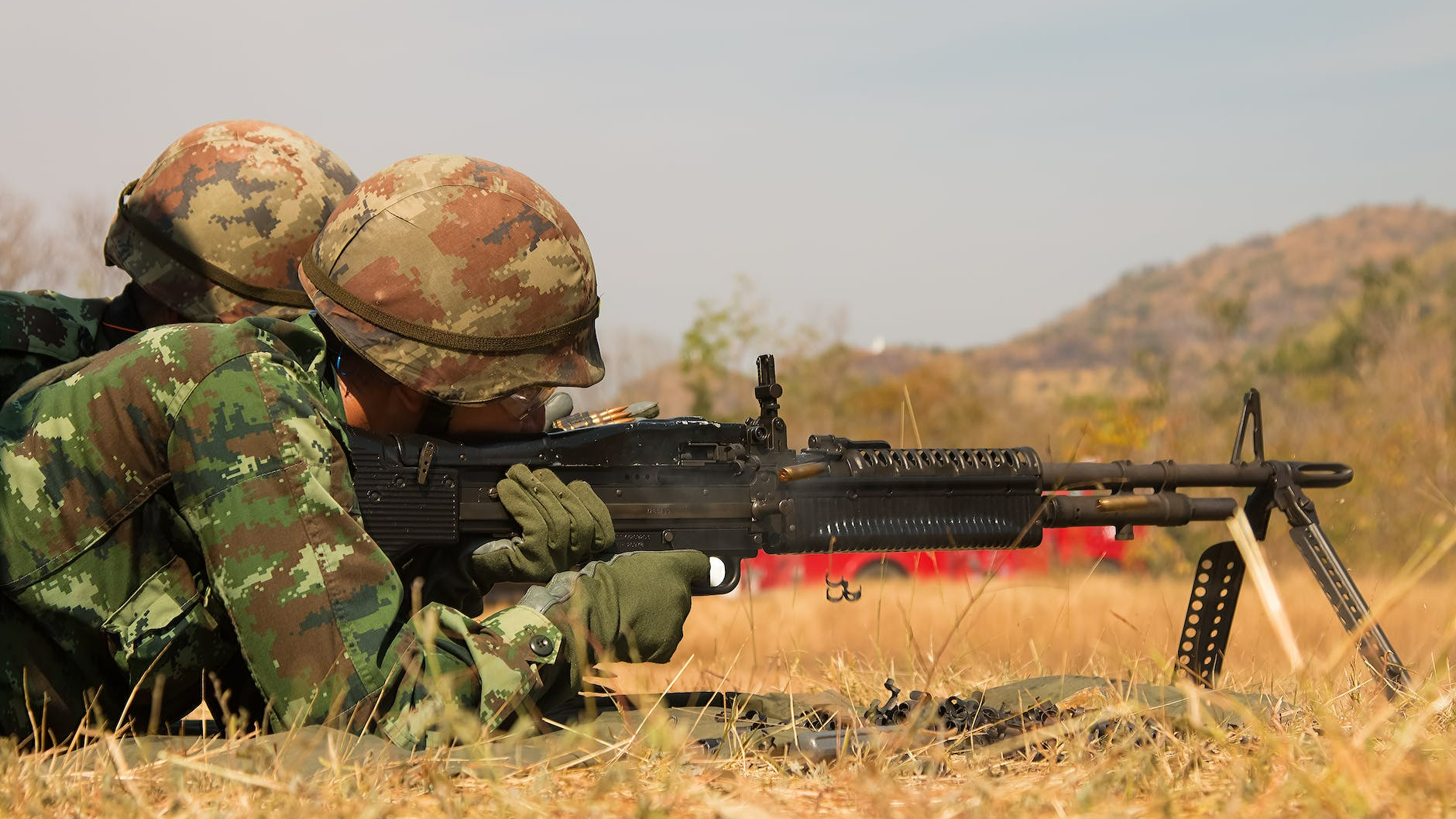man lying forward using rifle at the field during day