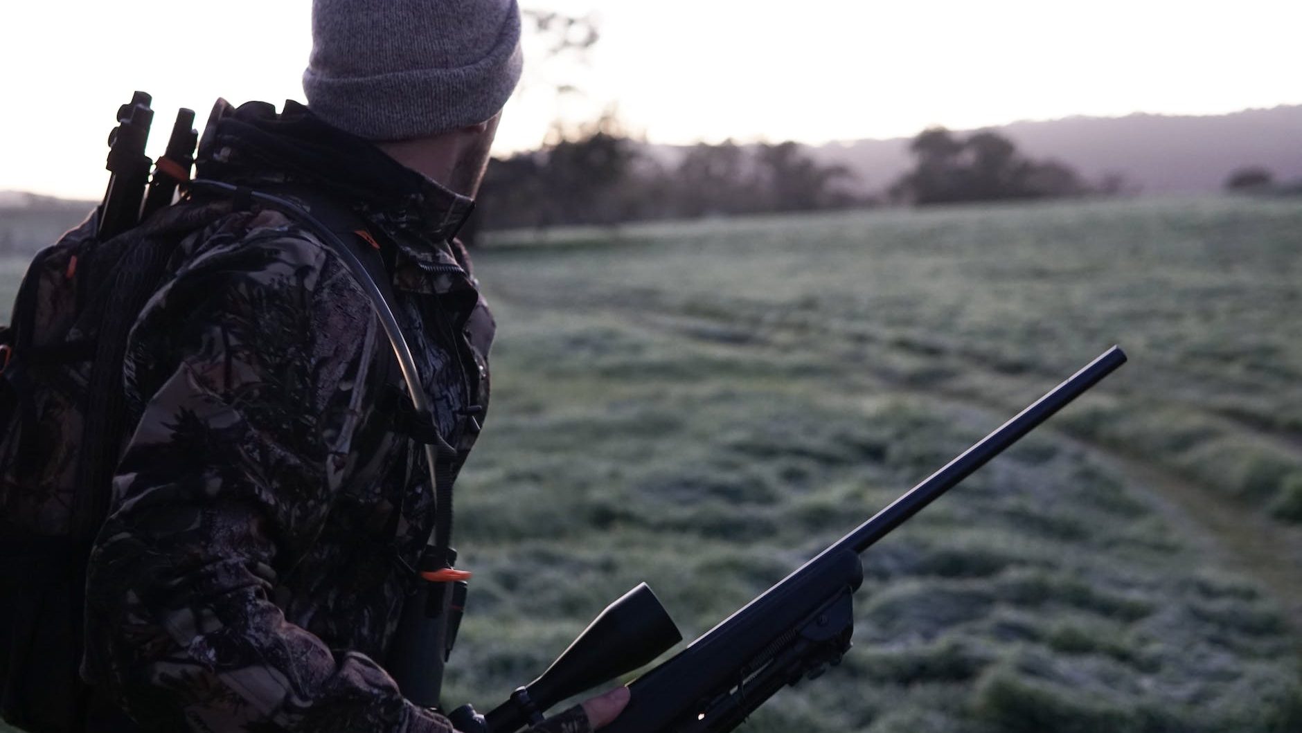 man wearing gray and black camouflage jacket holding rifle walking on grass field